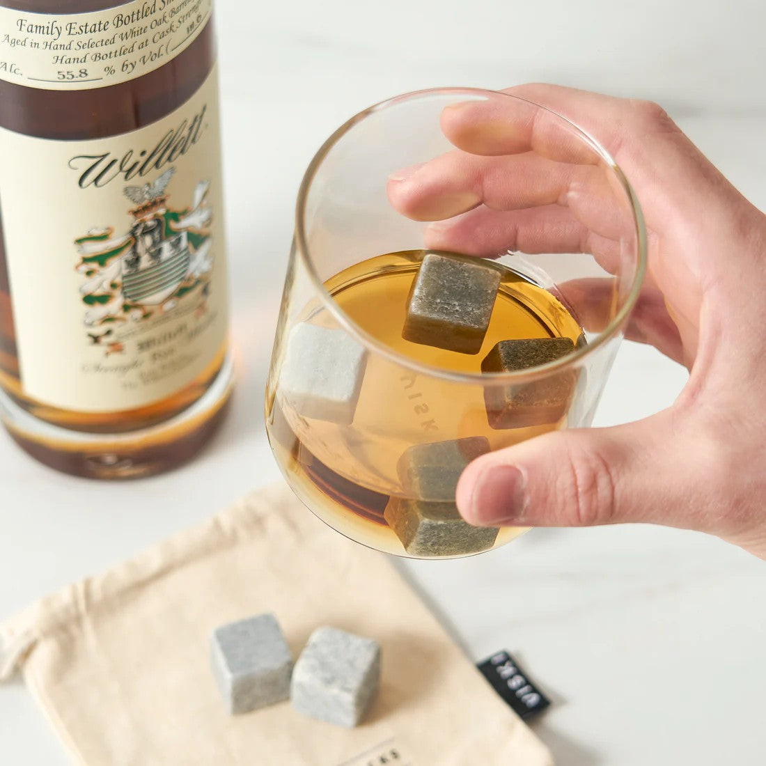 Hand holding a glass of whiskey with whiskey stones, next to a bottle of Wilder whiskey.