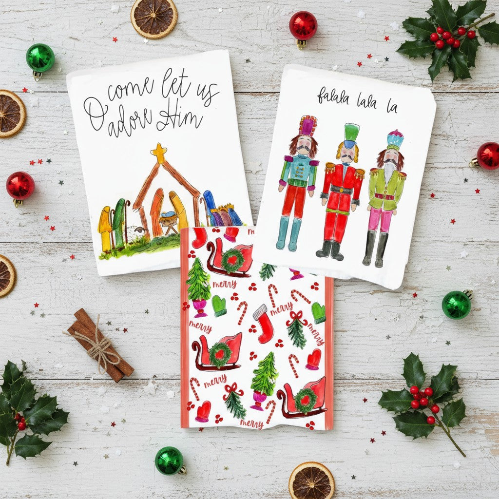 A collection of three festive Christmas tea towels displayed together, showing the Nutcracker, Nativity, and All Things Christmas designs.