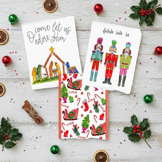 A collection of three festive Christmas tea towels displayed together, showing the Nutcracker, Nativity, and All Things Christmas designs.