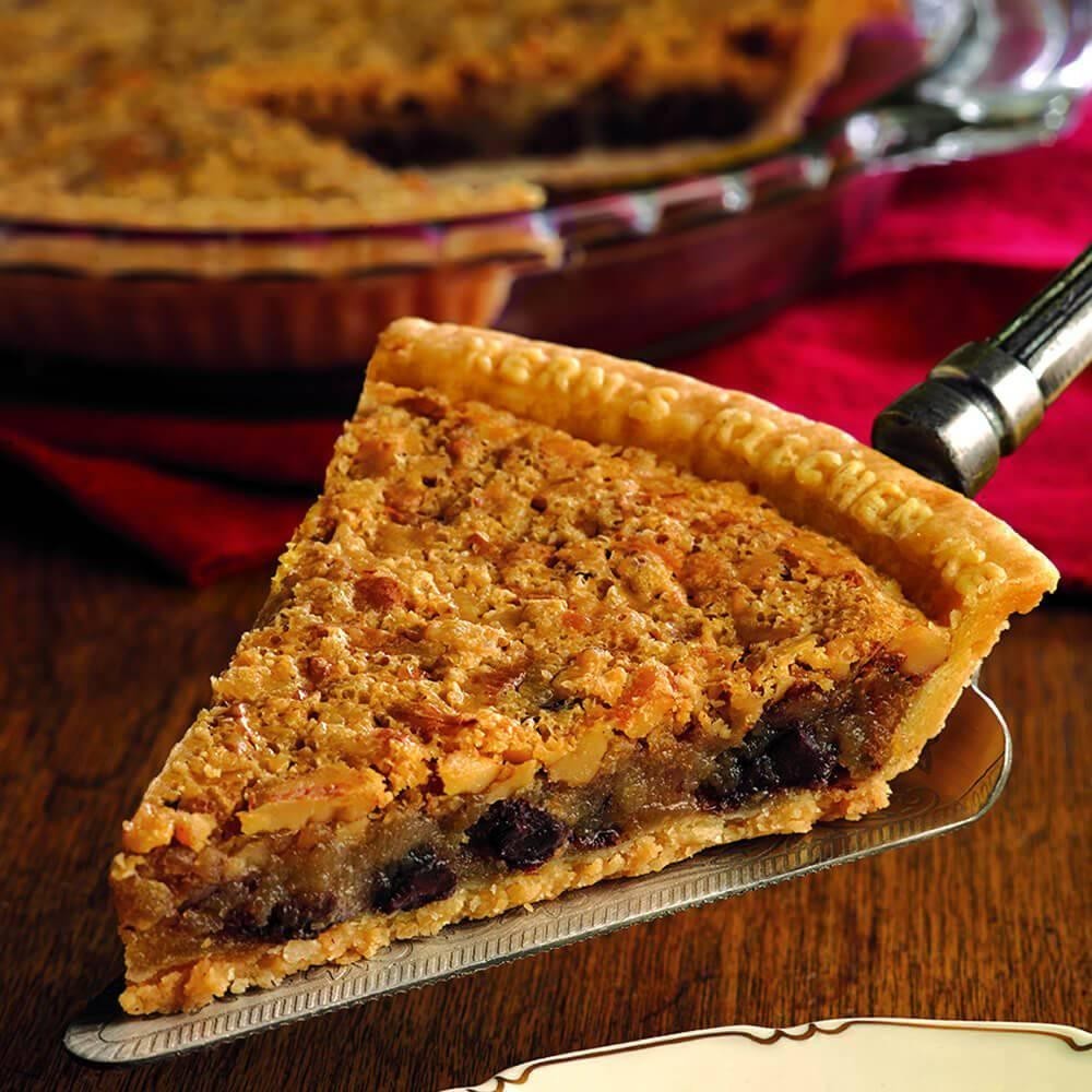Slice of pecan pie on a spatula with a whole pie in the background