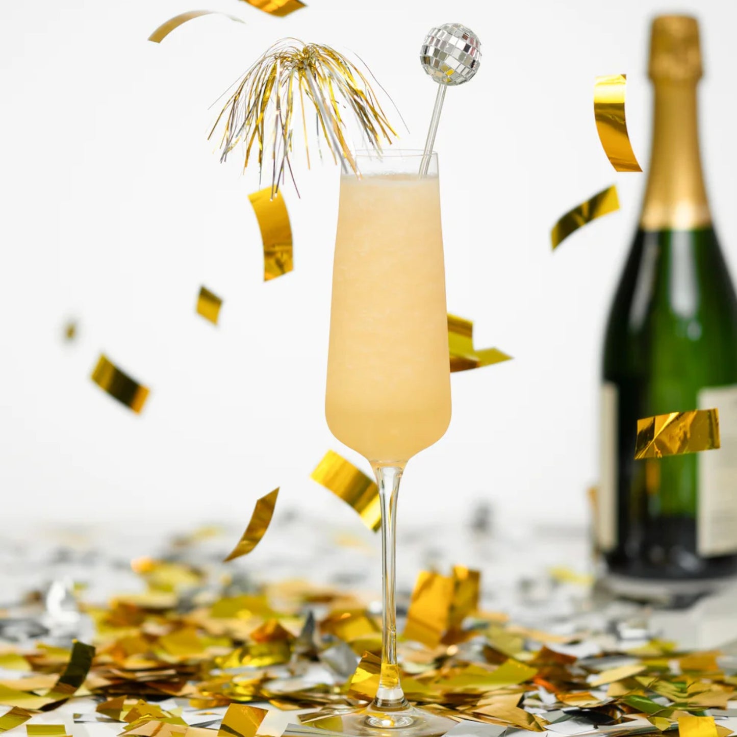 Champagne flute with a cocktail and bottle of champagne on a table with confetti.