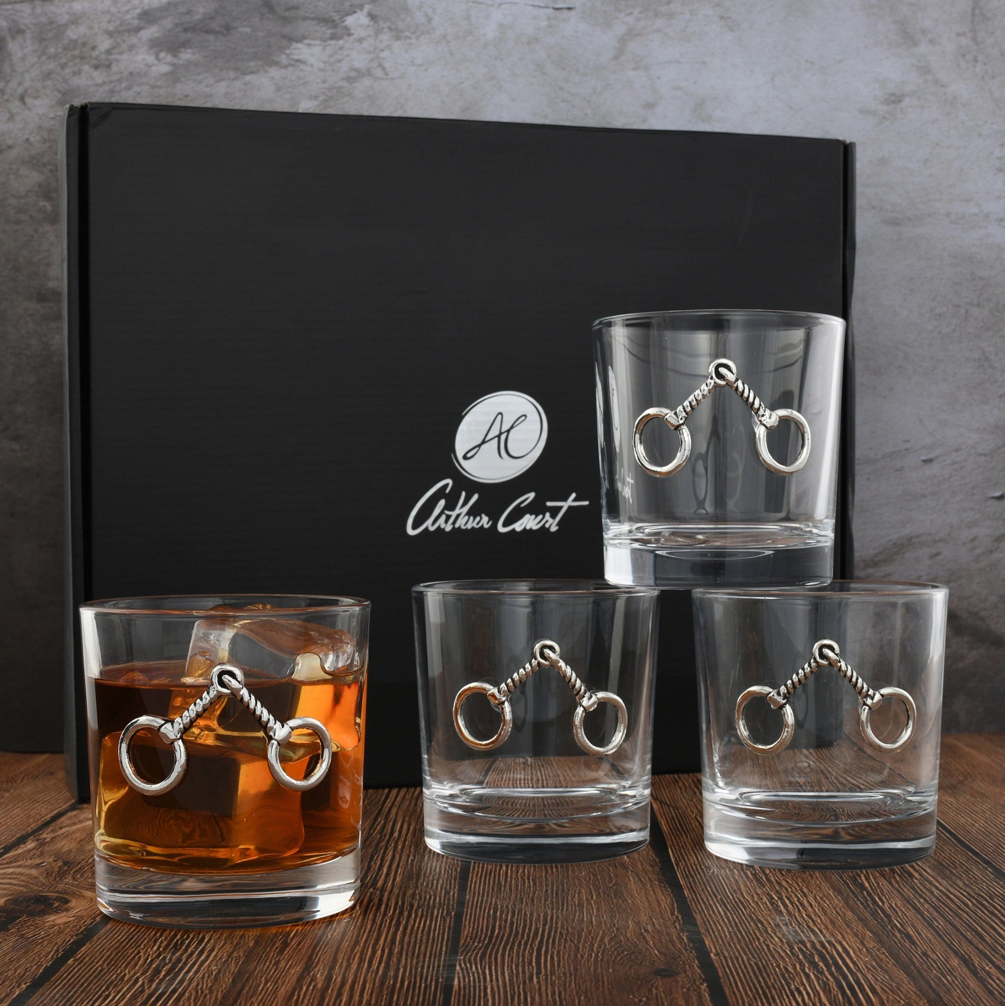 Set of four elegant 10 oz equestrian bit bar glasses on a wooden surface, with a black box in the background.
