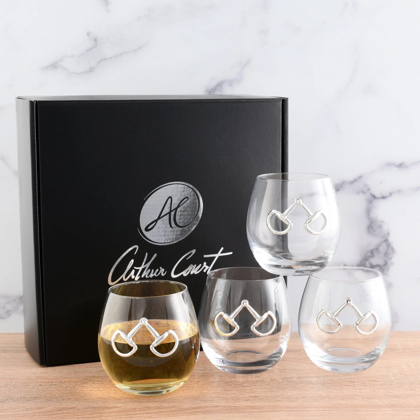 Set of four equestrian bit stemless wine glasses with 'Arthur Court' branding on a marble background