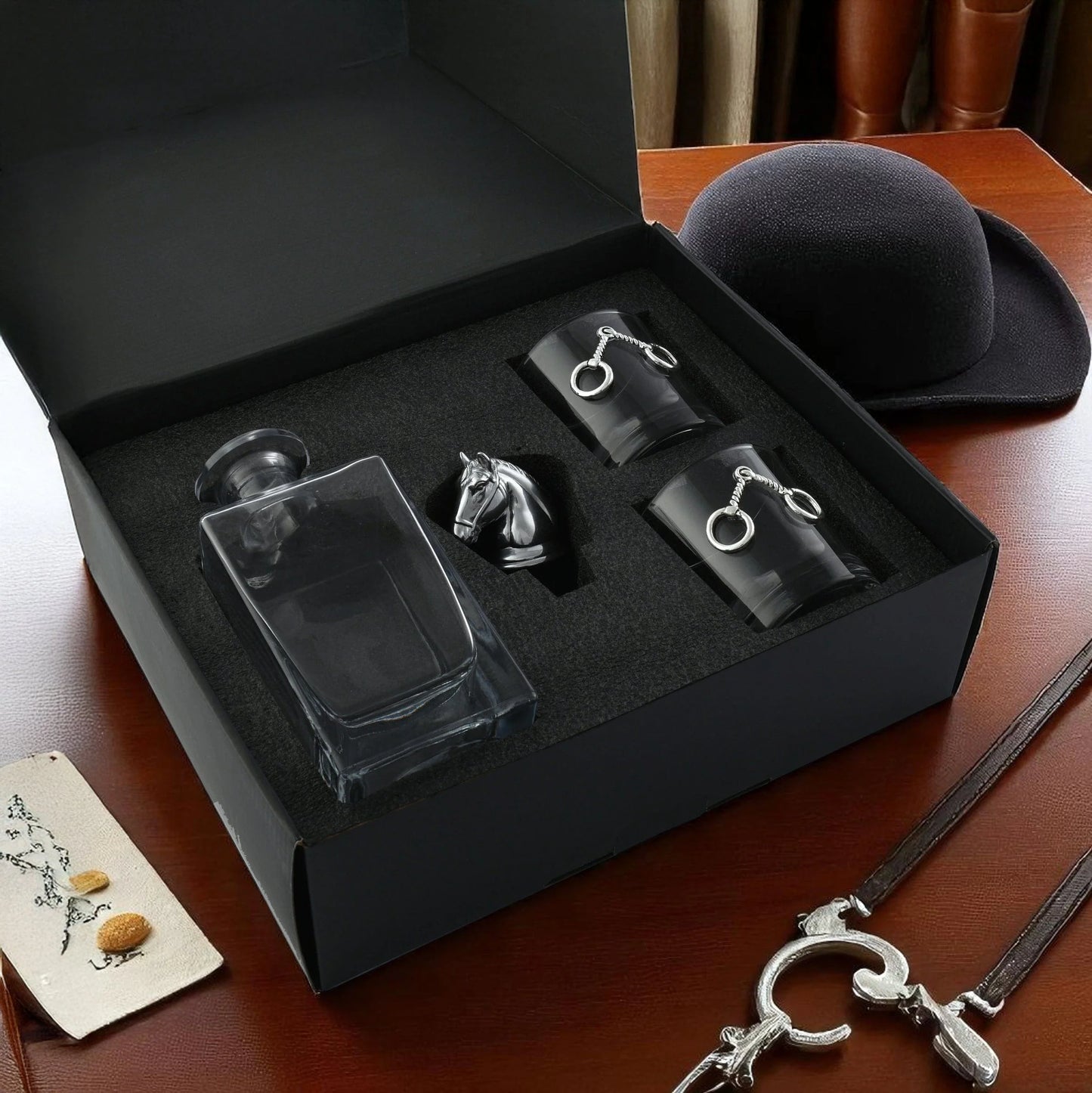 Set of black and silver keychains and a glass flask in a black box on a wooden surface.