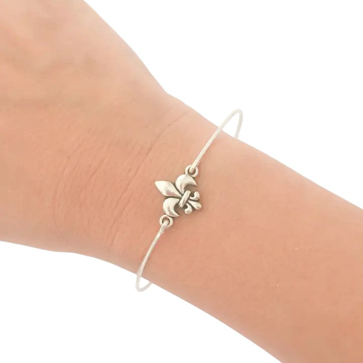 A silver fleur de lis bangle bracelet shown on a woman's wrist.