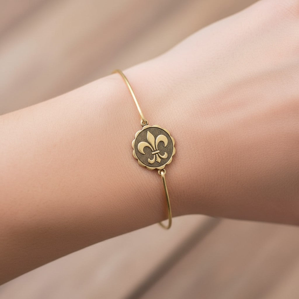 A gold fleur de lis coin bangle shown on a woman's wrist.