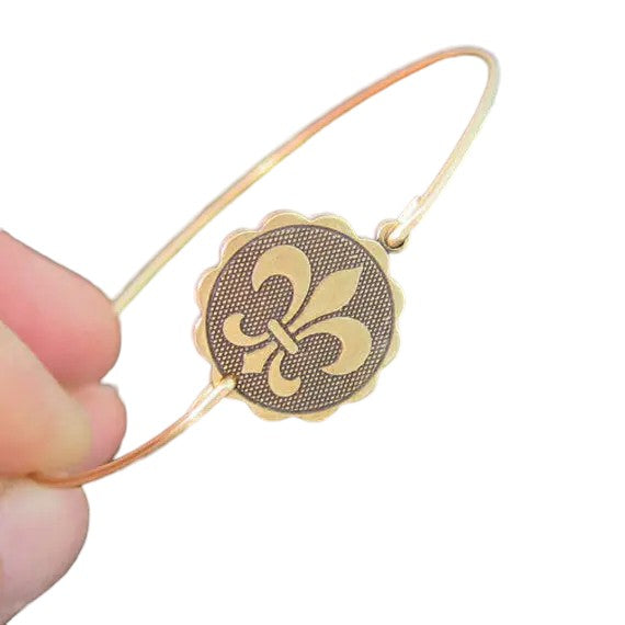 A close-up of the detailed fleur de lis emblem on the gold-tone coin charm of the bangle.