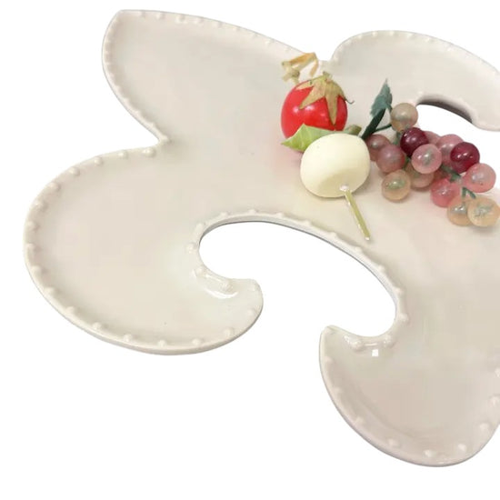 Decorative white dish shaped like a Fleur-de-Lis with food on a white background