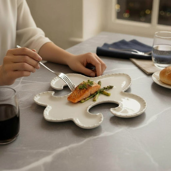 A meal of salmon and asparagus served on a white Fleur-de-Lis shaped melamine plate.