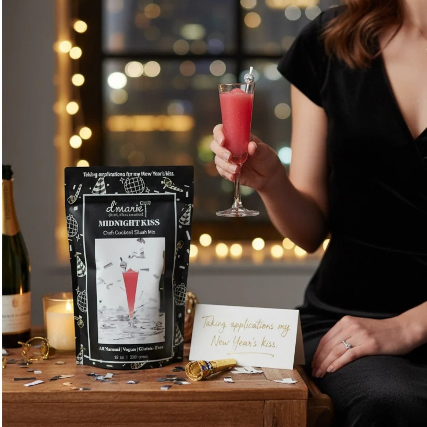 Person holding a cocktail with démaré Midnight Kiss cocktail mix and New Year's Eve decorations.