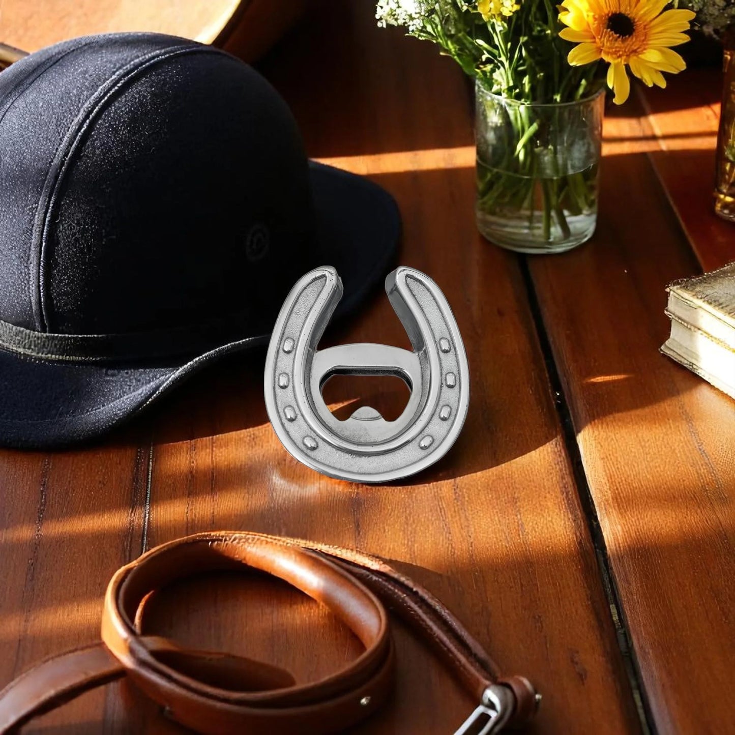 Horseshoe-shaped bottle opener on a wooden surface with a hat, belt, and flowers in the background.
