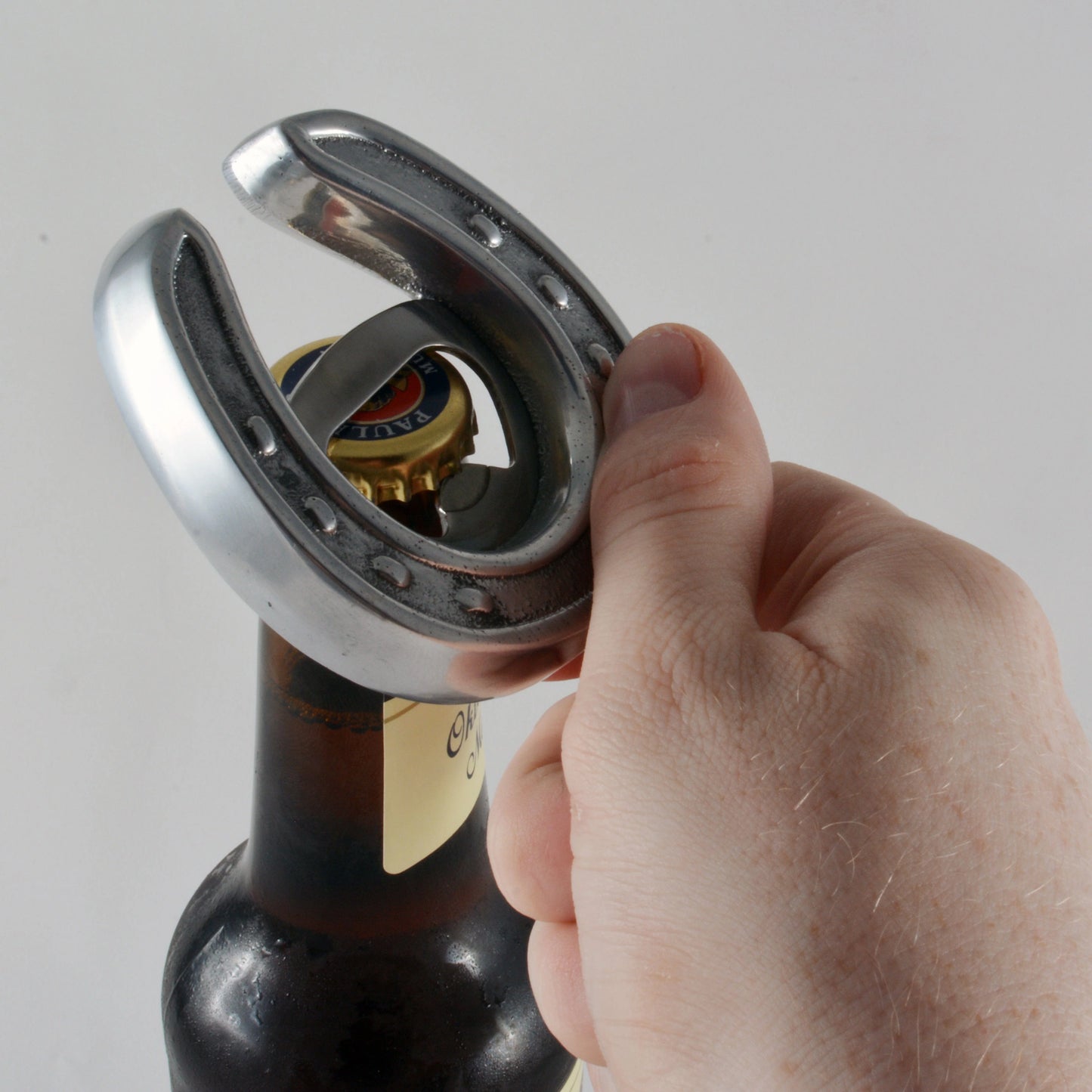 Hand using a bottle opener on a bottle with a plain background