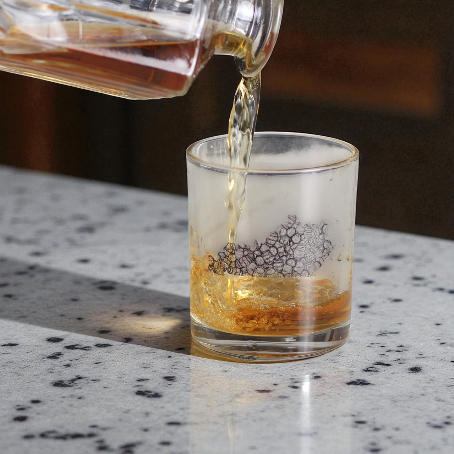 Alcohol being poured from a decanter into a glass on a speckled countertop.