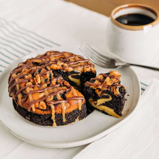 Chocolate cake with pecan topping on a plate with a cup of coffee.