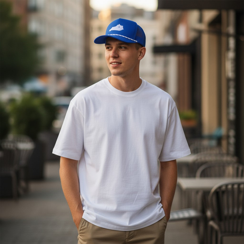 Man wearing a blue of the Lexington, KY state hat, showing the pre-curved visor and white t-shirt standing outdoors with blurred background