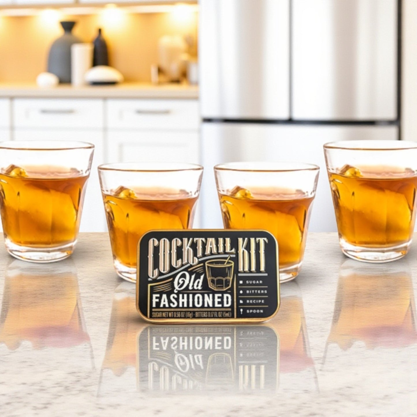 A finished Old Fashioned cocktail in a glass beside the open kit tin on a kitchen counter.