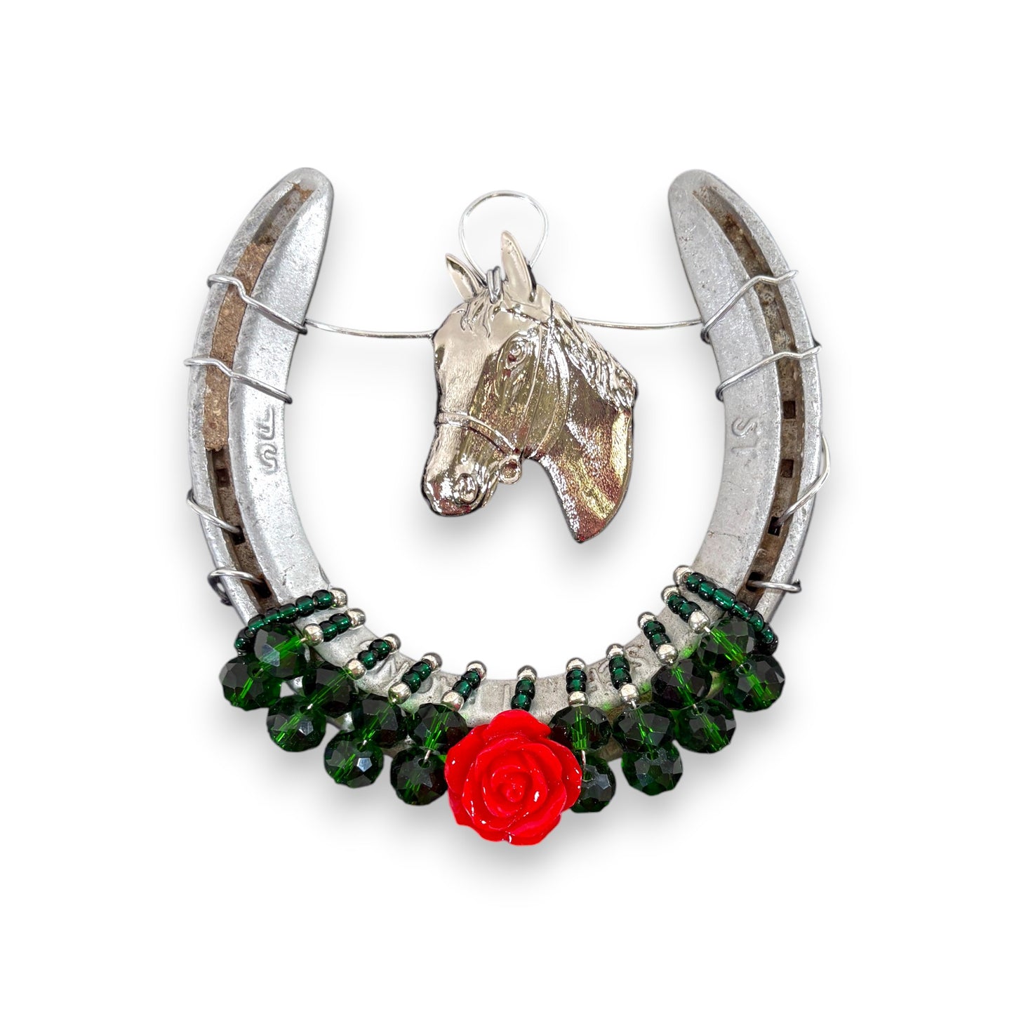The authentic metal horseshoe adorned with a silver horsehead charm and a single rose, hanging on a wall.