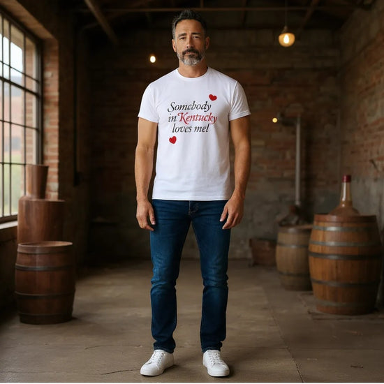 Man wearing a white t-shirt with text and red hearts in a rustic setting with wooden barrels.