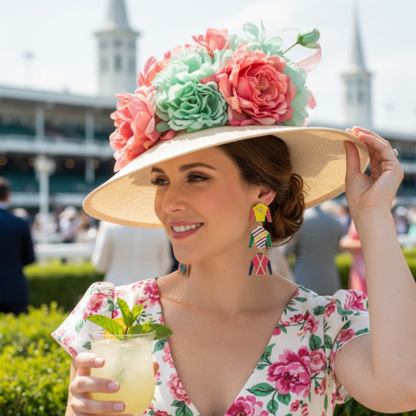 A woman wearing the Triple Crown Jockey Silk Multi Earrings at an outdoor event, paired with a floral dress and hat.