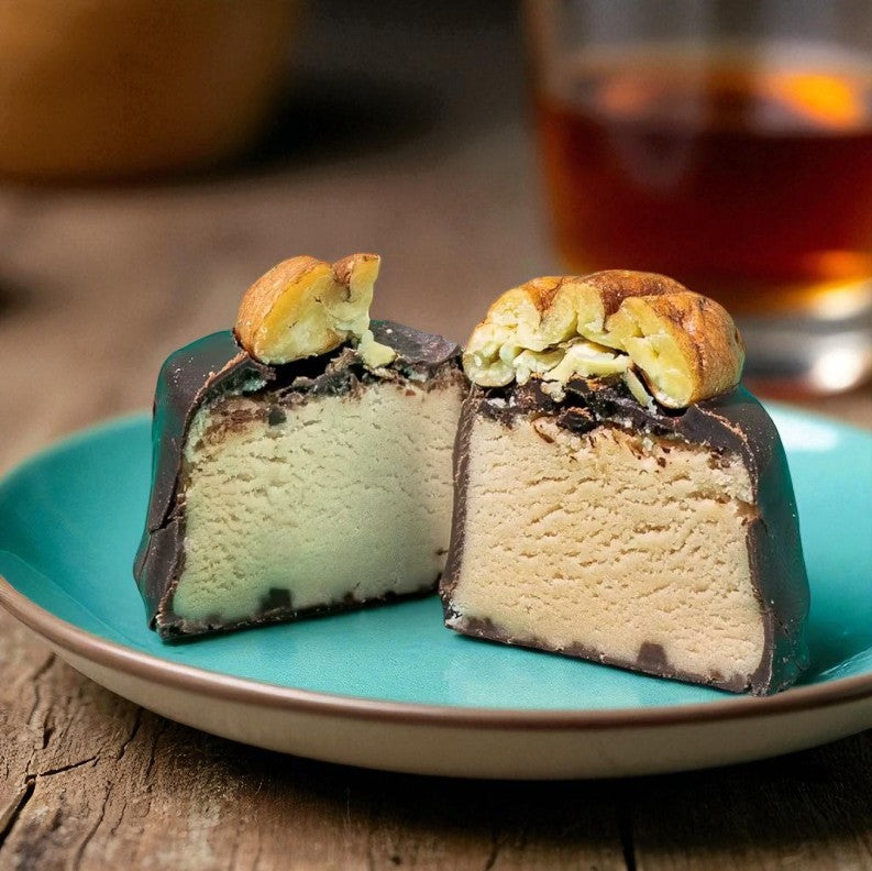 Two pieces of ice cream cake on a turquoise plate with a glass of amber liquid in the background.