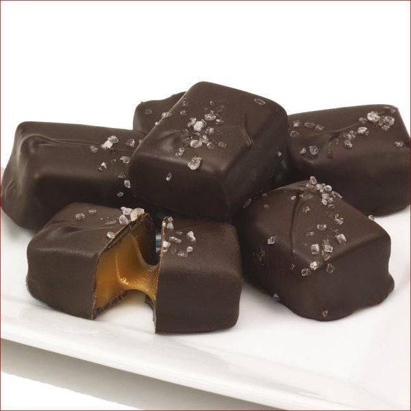 Dark chocolate caramels with a few sprinkled with sea salt on a white plate.