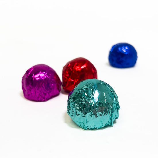 Four colorful chocolate truffles in foil on a white background