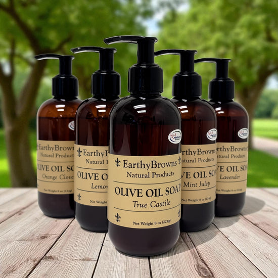 Five bottles of Earthy Browns Natural Products olive oil soap on a wooden surface with a natural background.