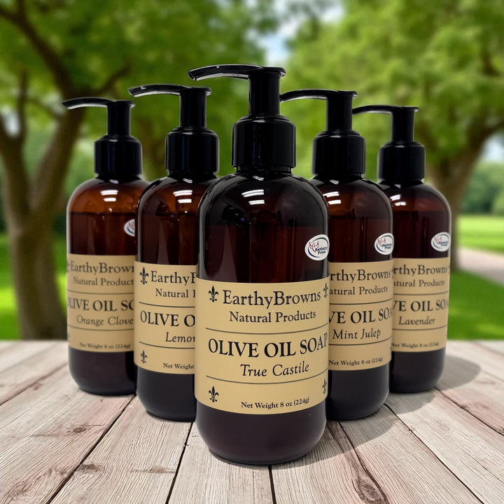 Five bottles of Earthy Browns Natural Products olive oil soap on a wooden surface with a natural background.