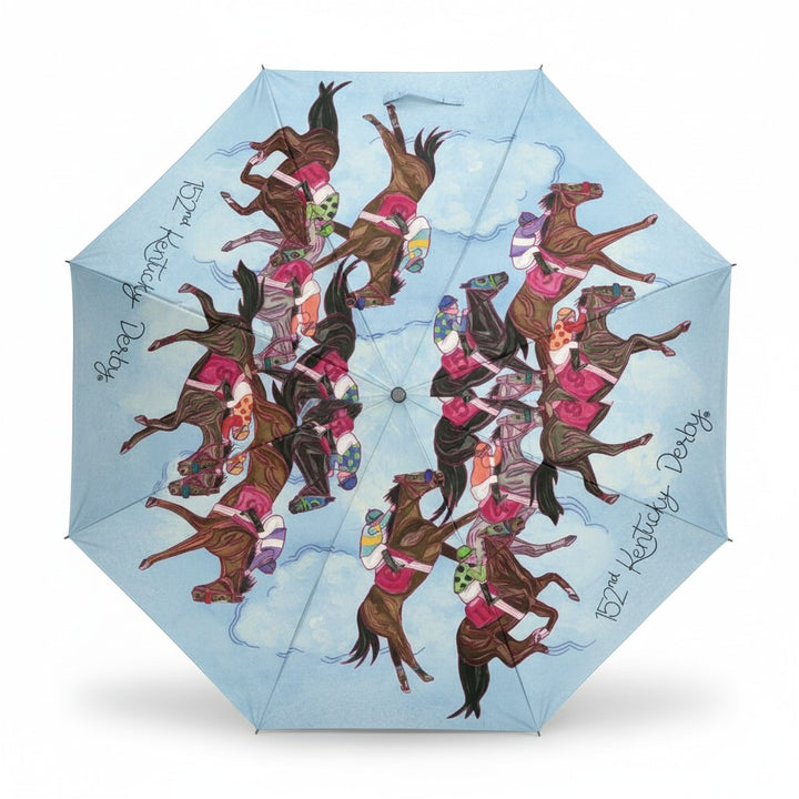 An open light blue umbrella seen from above, showcasing the colorful, circular pattern of racehorses and jockeys from the Art of the Derby 152 collection.