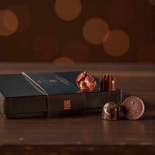 A beautiful gift box of 16 assorted artisan chocolates on a dark wooden surface.