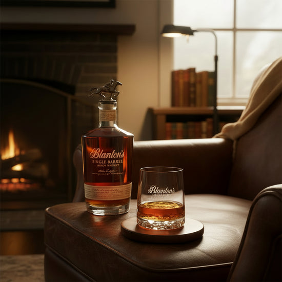  The Blanton's rocks glass sitting on a leather armchair next to a bottle of Blanton's Single Barrel Bourbon by a warm fireplace.
