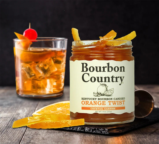 Bourbon Country orange twist jar with a cocktail garnished with an orange peel and cherry on a wooden surface.