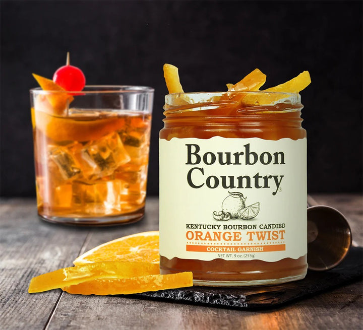Bourbon Country orange twist jar with a cocktail garnished with an orange peel and cherry on a wooden surface.