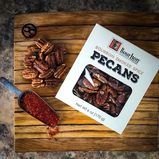 Bourbon Smoked Spice Pecans packaging on a wooden cutting board with pecans and a scoop of seasoning.