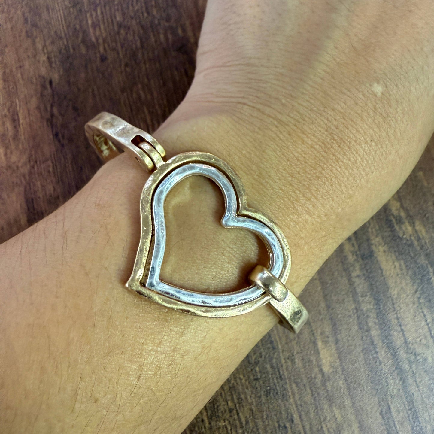 Gold and silver heart-shaped bracelet on a wrist with a wooden background