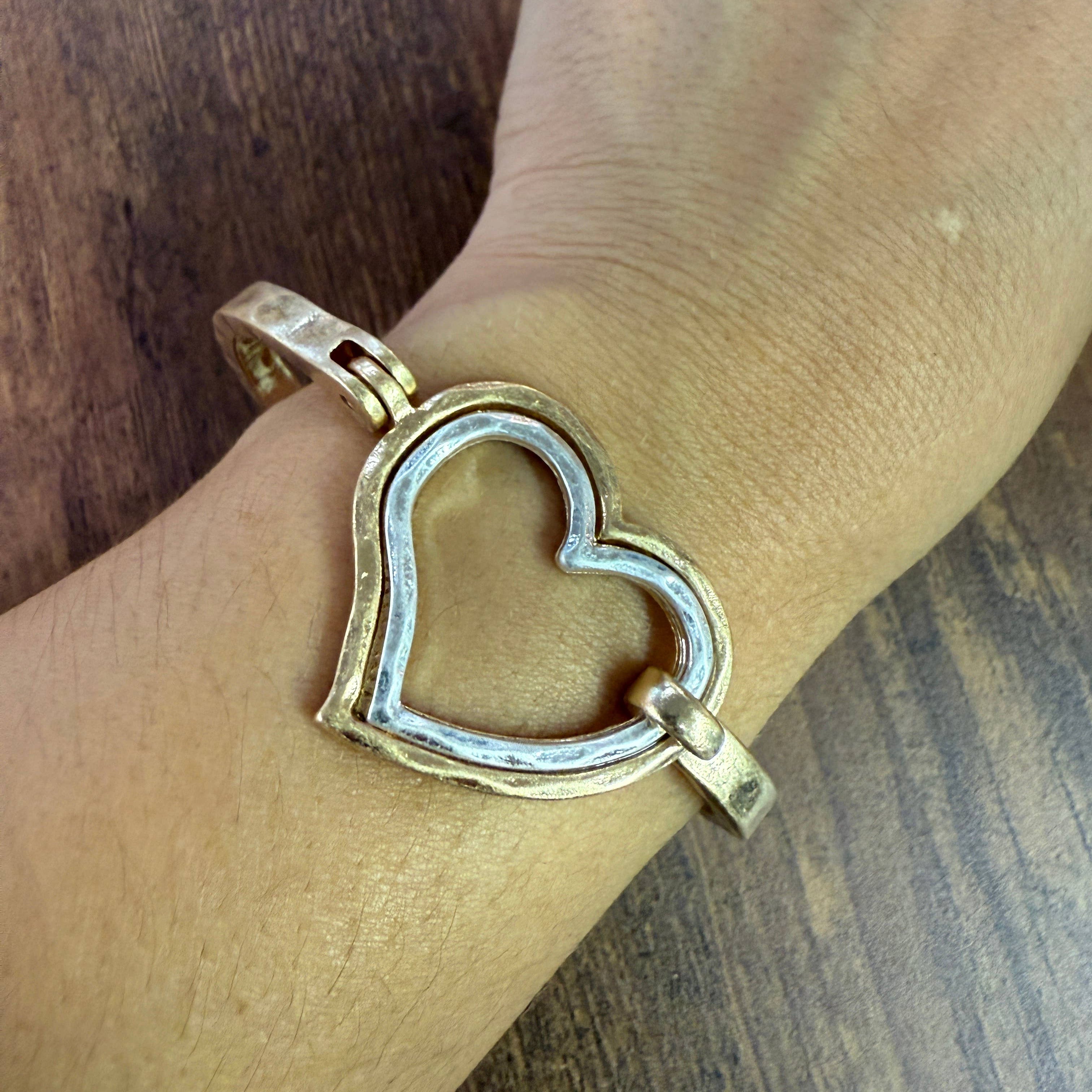 Gold and silver heart-shaped bracelet on a wrist with a wooden background