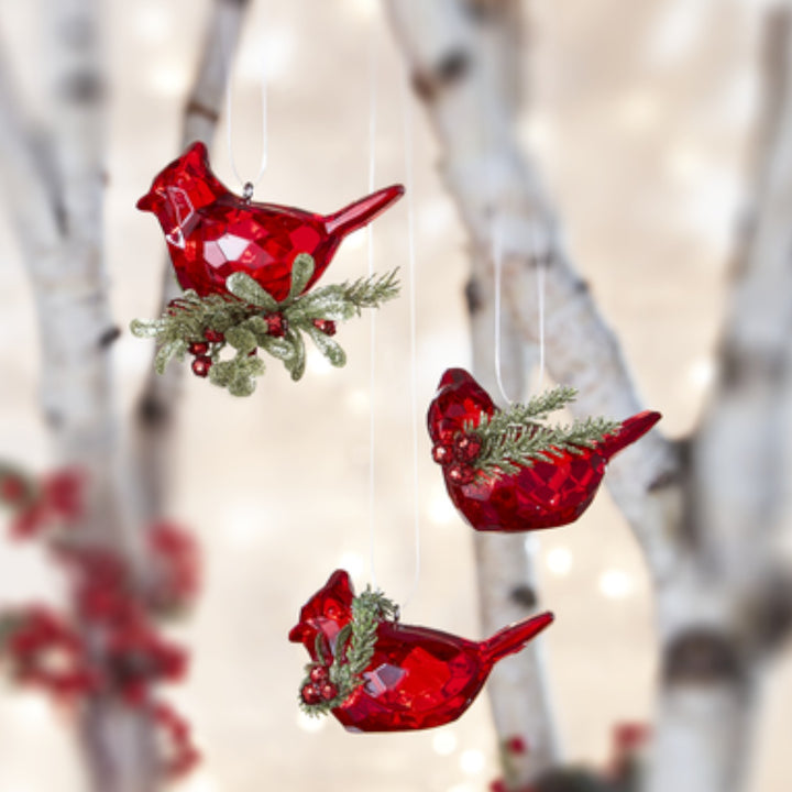 Red bird-shaped Christmas ornaments with greenery against a blurred natural background