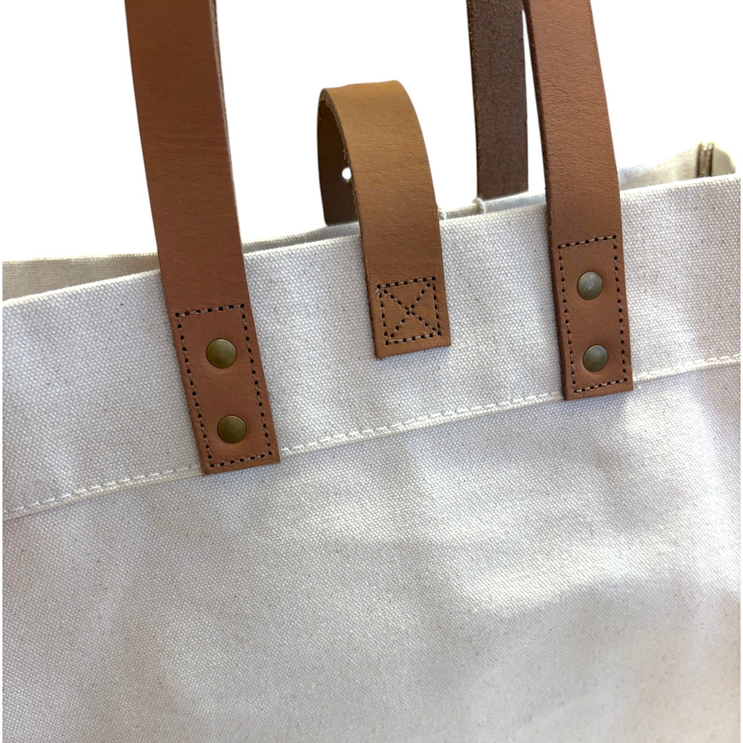 Close-up of a tote bag with brown leather handles and straps.