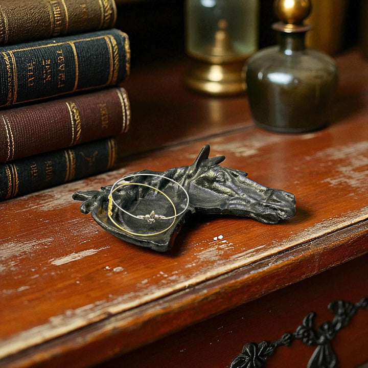 Bronze horse head jewelry holder on a wooden surface with books and decorative items.