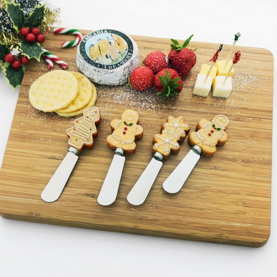 A festive holiday charcuterie board with cheeses, crackers, and cookie-handled spreaders.