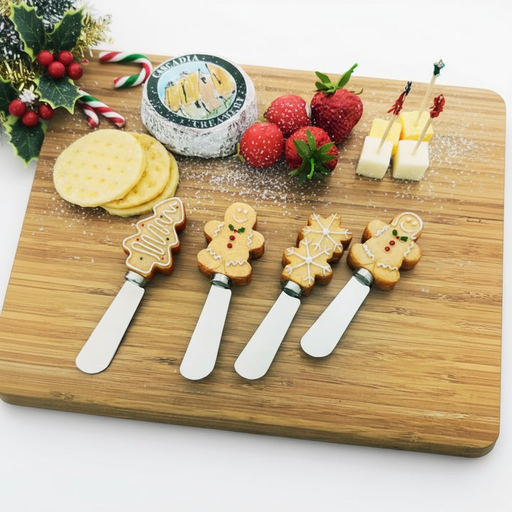 A festive holiday charcuterie board with cheeses, crackers, and cookie-handled spreaders.