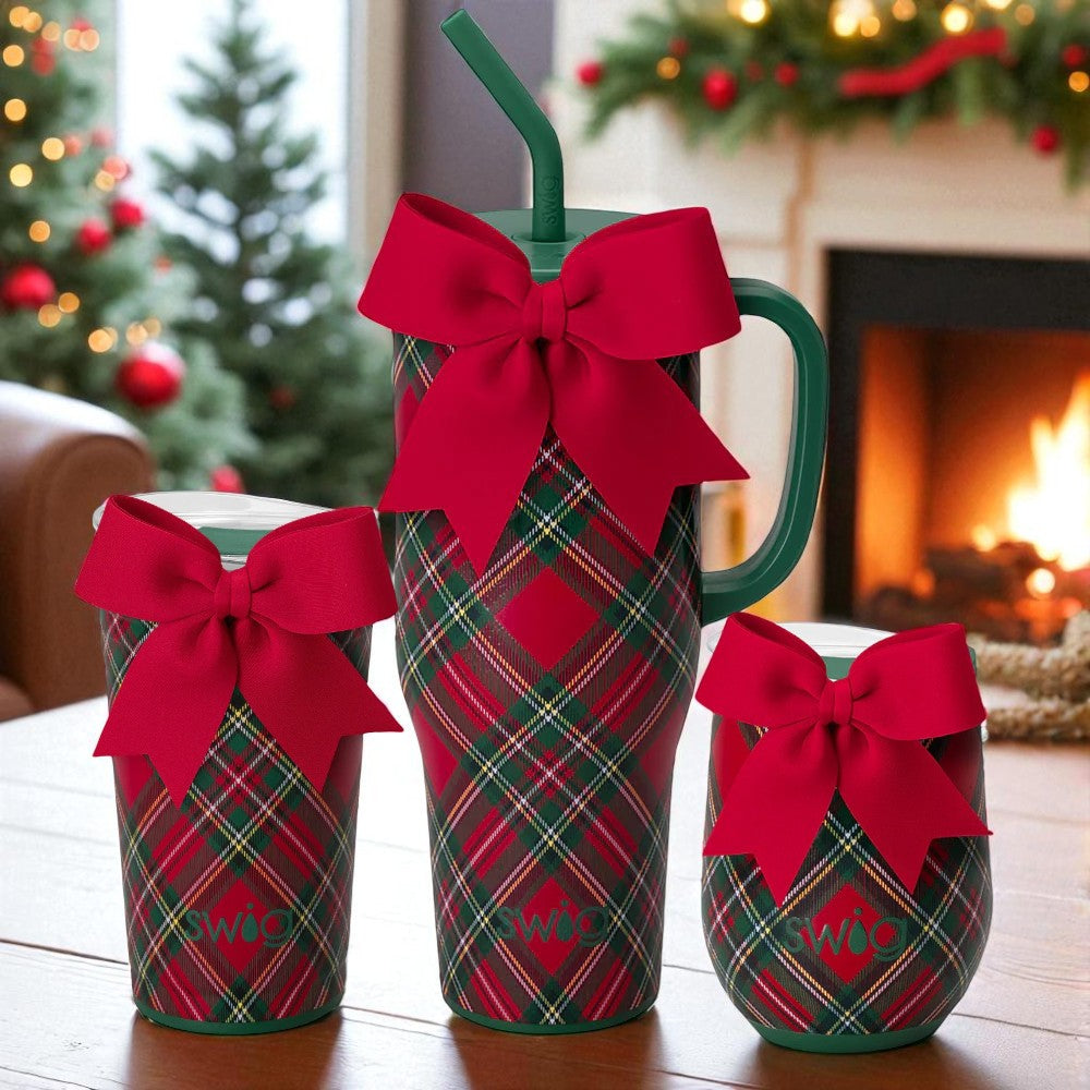 Trio of Swig Christmas Plaid drinkware—40oz mega mug with handle and straw, 24oz party cup, and 12oz stemless wine—styled with red bows in a cozy holiday scene.