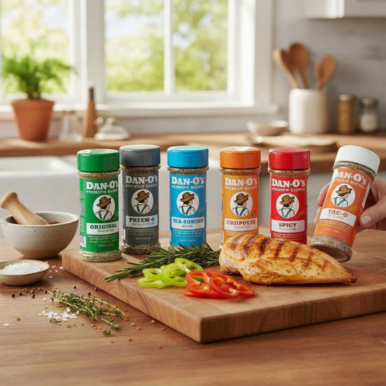 Collection of Dan-O's seasoning bottles on a kitchen counter with ingredients and a hand holding a bottle.