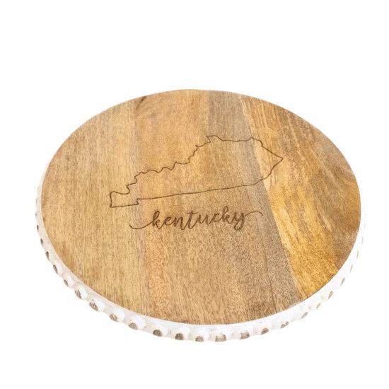 A round wooden serving board with an engraved Kentucky outline on a white background.