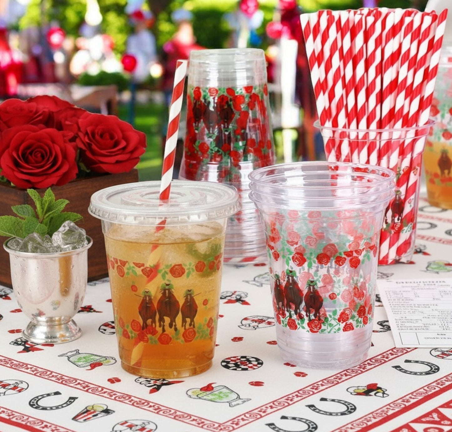 A clear 12oz plastic cup featuring a horse racing and red rose design, complete with a clear flat lid and a red-and-white striped paper straw, placed next to a neat stack of matching cups.