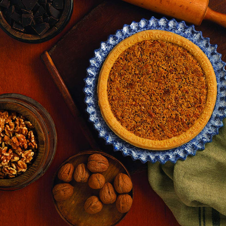 Carrot pie with a blue ceramic dish on a wooden table, surrounded by walnuts and a green towel.