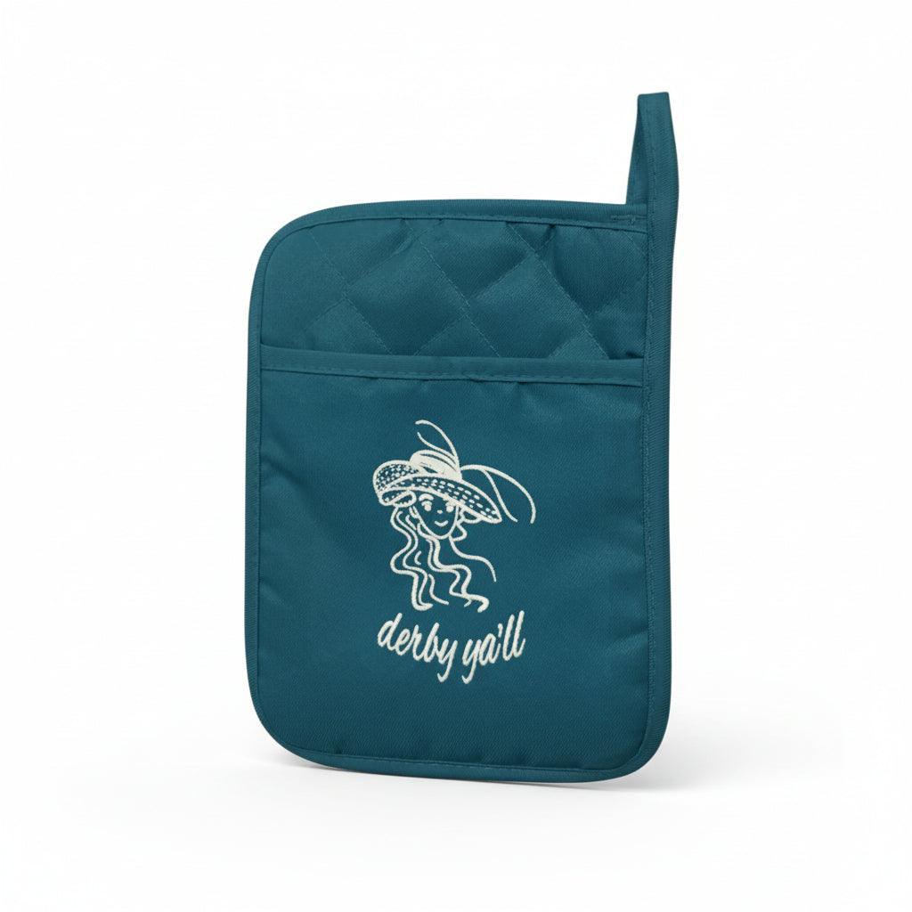 Close-up of a teal pot holder featuring a white embroidered design of a woman in a large hat with the text "derby y'all."