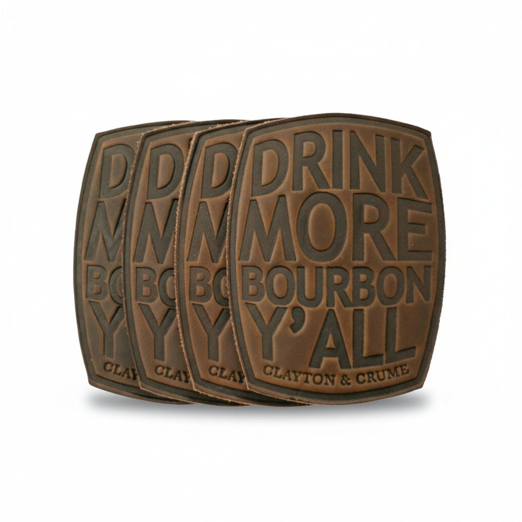  A set of four brown Horween leather coasters arranged on a table, featuring the debossed phrase "Drink More Bourbon, Y'all."