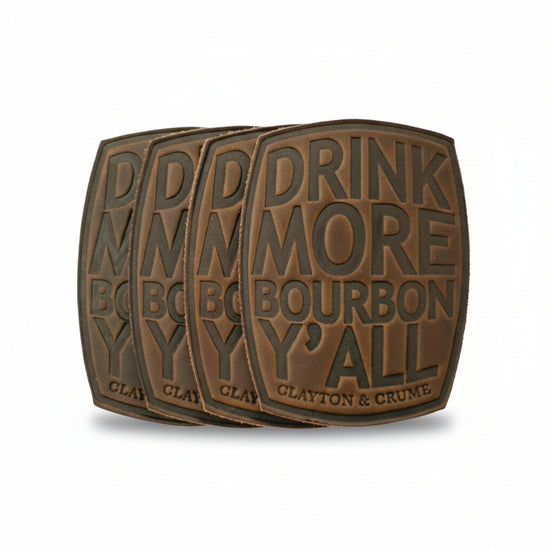  A set of four brown Horween leather coasters arranged on a table, featuring the debossed phrase "Drink More Bourbon, Y'all."