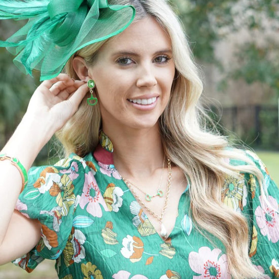 Woman wearing a green floral dress and hat and the Navy Eclipse Rhinestone Enamel Horsebit Earrings, with a blurred natural background